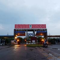Entrance gate of the Visakhapatnam Steel Plant at dusk, with a red signboard, wet road and two people on a motorcycle