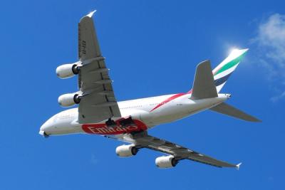 Emirates Airbus A380 jet in flight against a clear blue sky, seen from below.