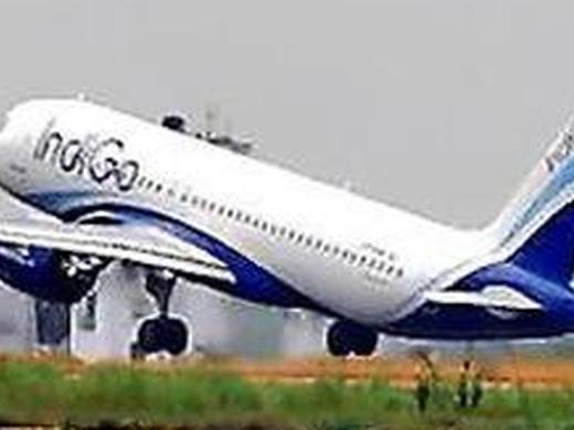 An IndiGo passenger jet lifting off from a runway, nose raised, with grass in the foreground and a grey sky behind
