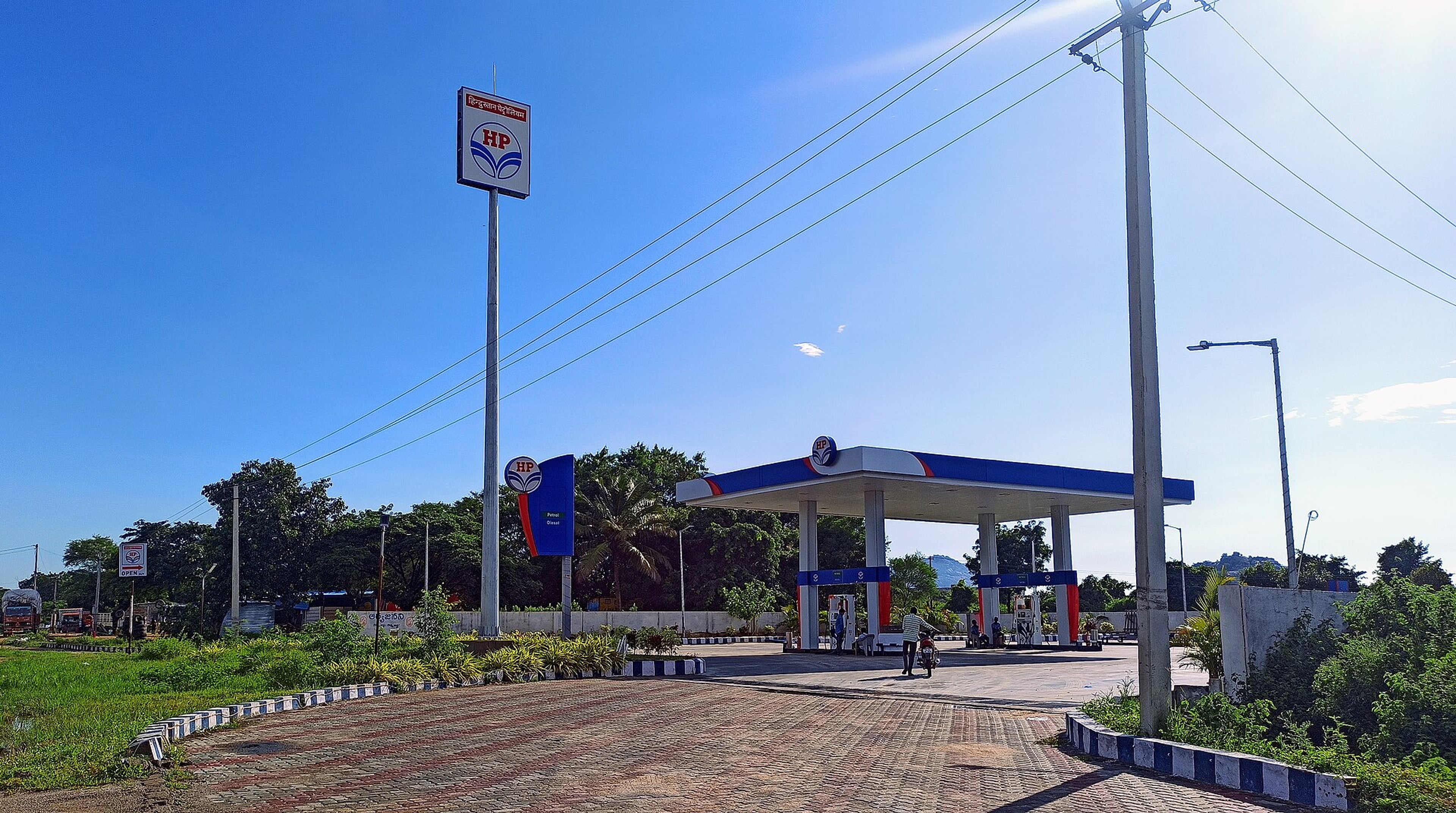 HP petrol station with a covered forecourt, fuel pumps and signboards under a clear blue sky.