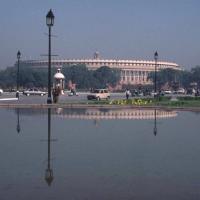Sansad Bhavan, the Parliament building in New Delhi, reflected in a pool with cars and people on the road.