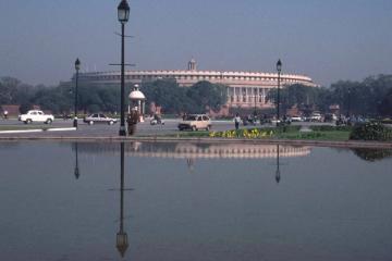 Sansad Bhavan, the Parliament building in New Delhi, seen across a reflecting pool with cars and pedestrians on the road