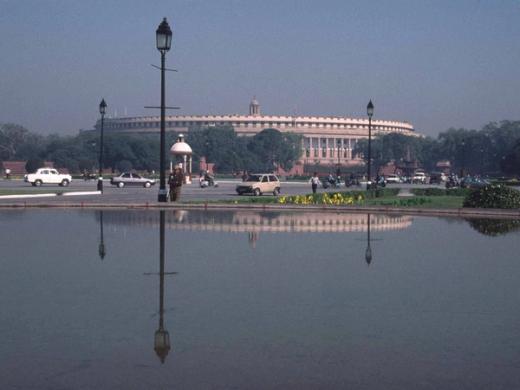 Sansad Bhavan, the Parliament building in New Delhi, reflected in a pool with cars and people on the road.