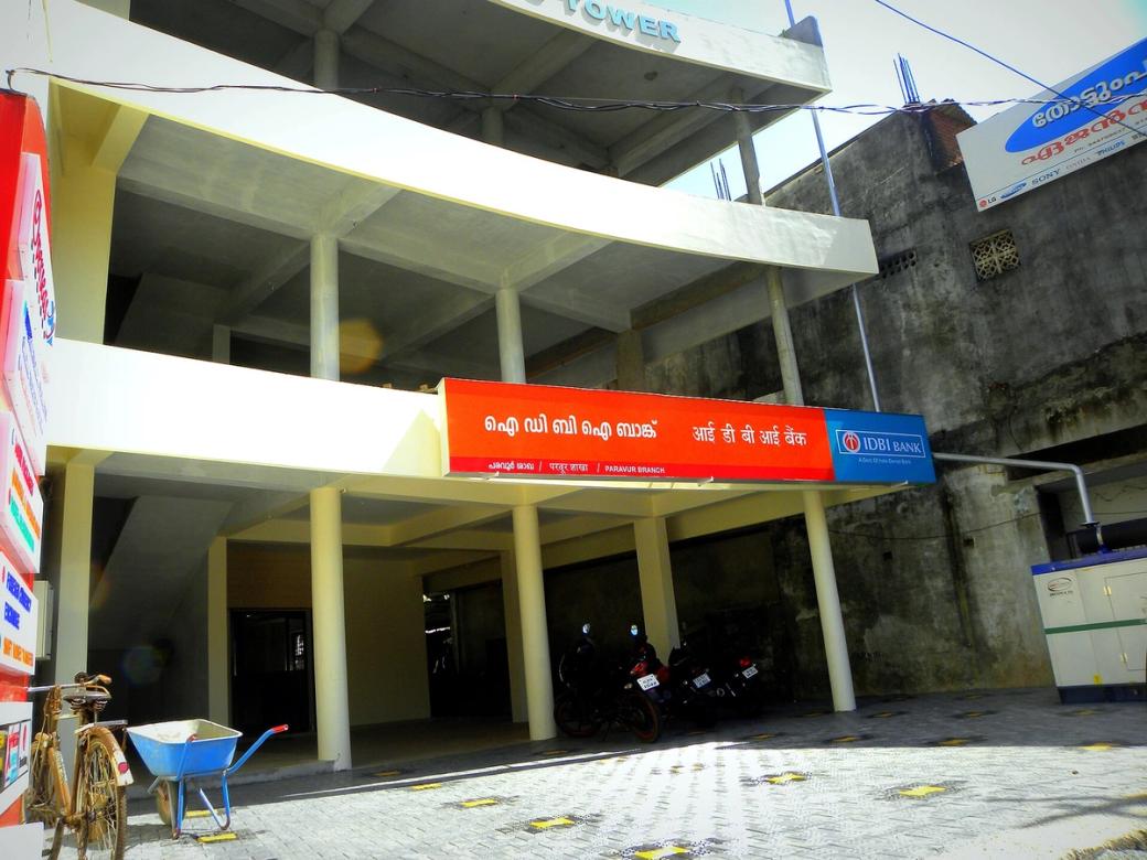 Exterior of an IDBI Bank branch with red and white signage, with motorbikes parked under a concrete building.