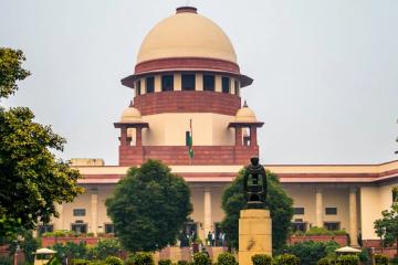 Central Wing of the Supreme Court of India with its domed tower, a statue on a plinth and people at the entrance.