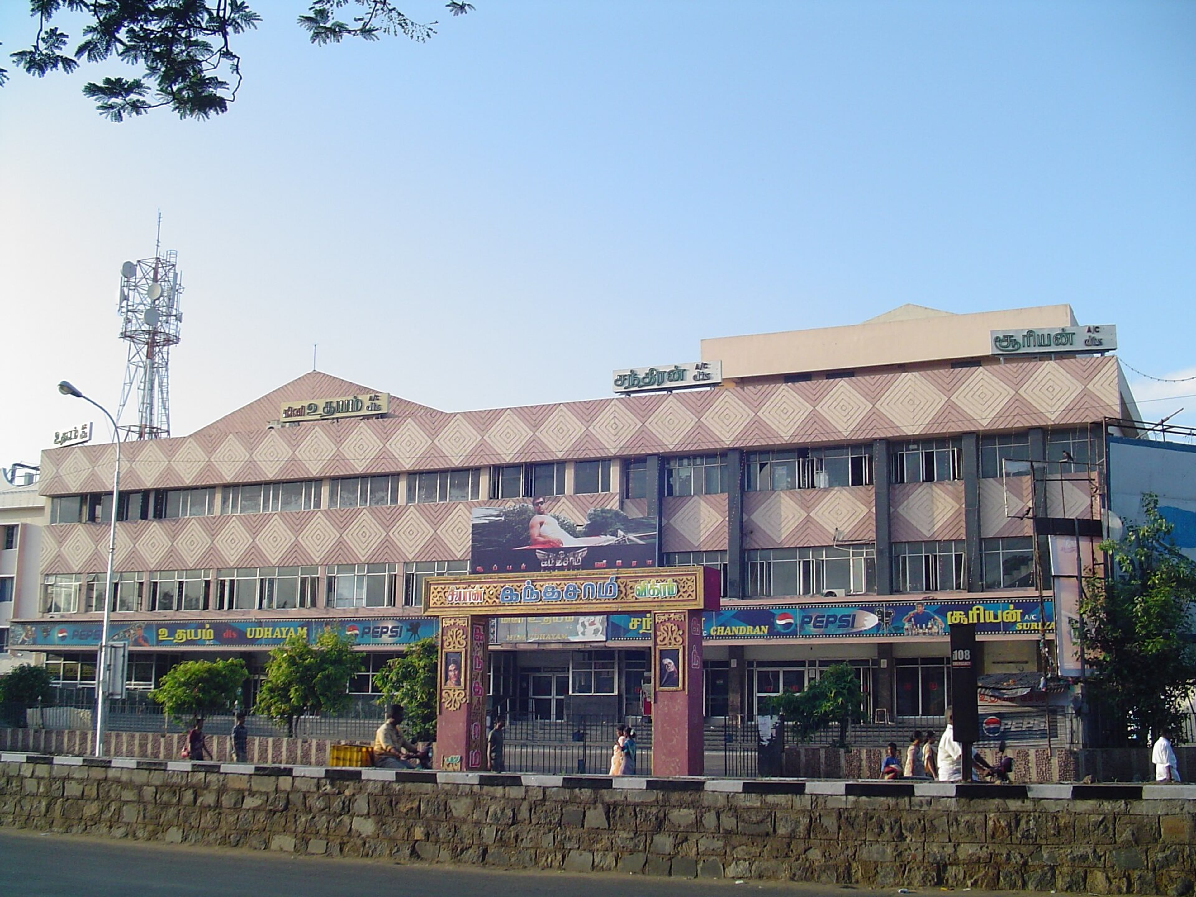 Facade of a multi-storey cinema hall with signboards, a film poster and pedestrians on the street