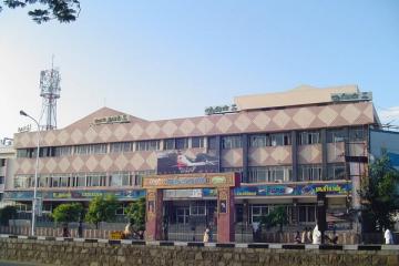 Facade of a multi-storey cinema hall with signboards, a film poster and pedestrians on the street