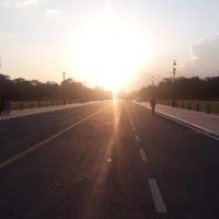 Evening sun over Kartavya Path in New Delhi, with lamp posts lining the road and a few pedestrians on the footpath.