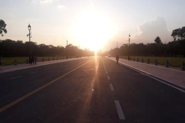 Evening sun over Kartavya Path in New Delhi, with lamp posts lining the road and a few pedestrians on the footpath.