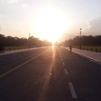Evening sun over Kartavya Path in New Delhi, with lamp posts lining the road and a few pedestrians on the footpath.
