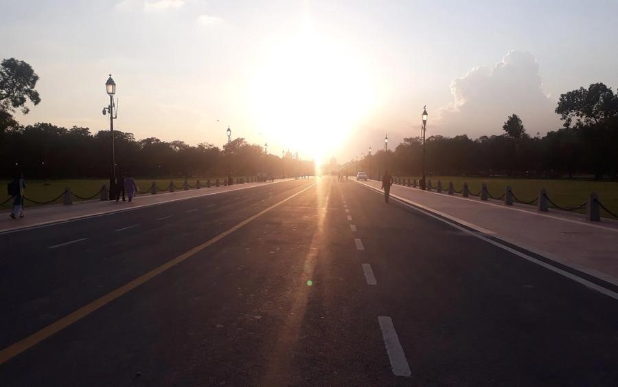 Evening sun over Kartavya Path in New Delhi, with lamp posts lining the road and a few pedestrians on the footpath.