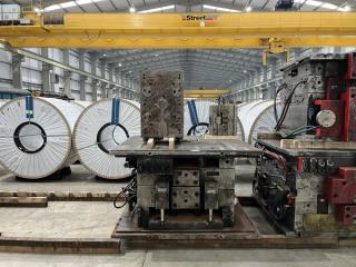 Large white-wrapped steel coils and metal industrial machinery on a factory floor under a yellow overhead crane