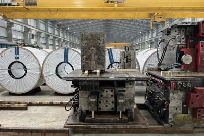 Large white-wrapped steel coils and metal industrial machinery on a factory floor under a yellow overhead crane