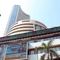 Curved high-rise tower and round building with a stock ticker band and a screen, seen from below with palm trees