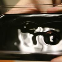 Dark ferrofluid blob in a clear tray, with fingers holding the tray at the edges