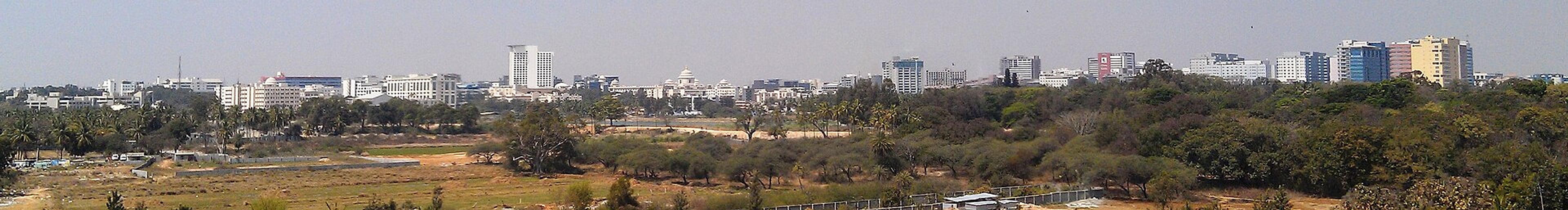 Hazy panoramic view of office and mid-rise buildings beyond trees and open ground in Bangalore.