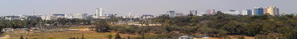 Hazy panoramic view of office and mid-rise buildings beyond trees and open ground in Bangalore.