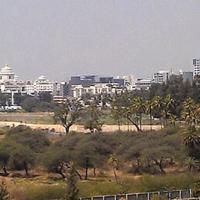 Hazy panoramic view of office and mid-rise buildings beyond trees and open ground in Bangalore.