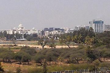 Hazy panoramic view of office and mid-rise buildings beyond trees and open ground in Bangalore.