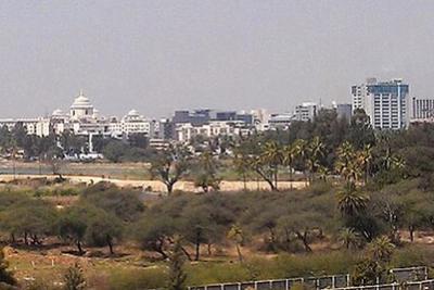 Hazy panoramic view of office and mid-rise buildings beyond trees and open ground in Bangalore.