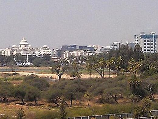 Hazy panoramic view of office and mid-rise buildings beyond trees and open ground in Bangalore.