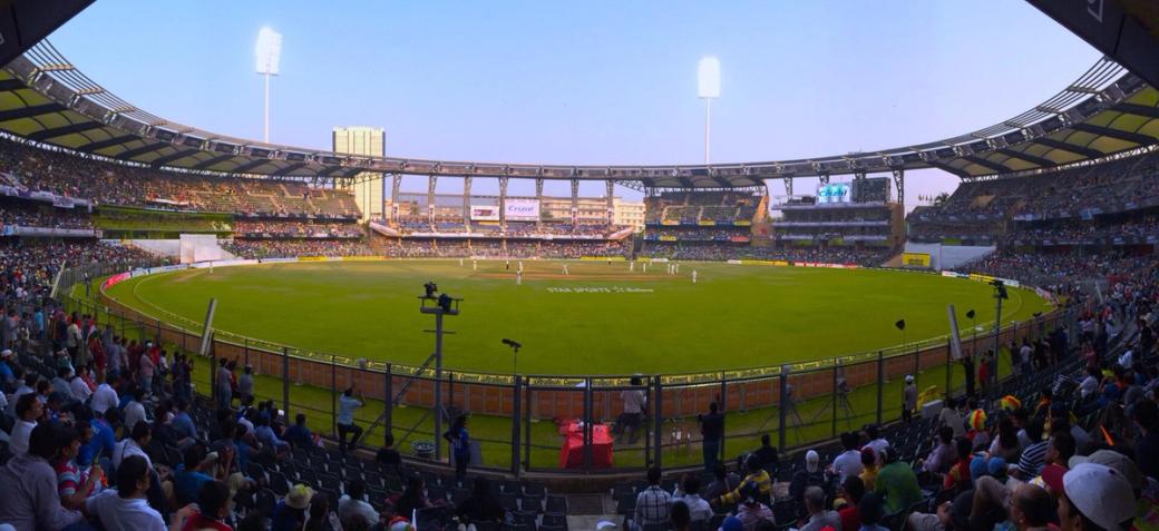 Panoramic view of Wankhede Stadium with crowded stands and players on the pitch in the evening light.