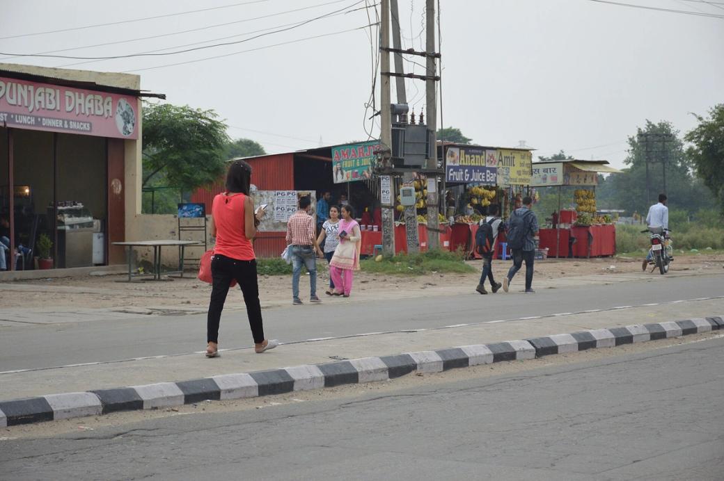 Woman in a red top and black trousers texting while walking along a roadside in Punjab, India.