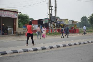 Woman in a red top and black trousers texting while walking along a roadside in Punjab, India.