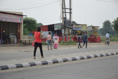Woman in a red top and black trousers texting while walking along a roadside in Punjab, India.