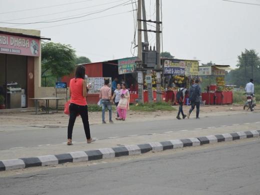 Woman in a red top and black trousers texting while walking along a roadside in Punjab, India.