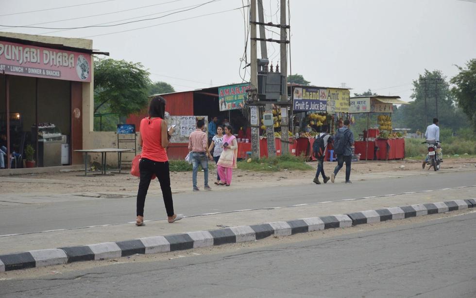 Woman in a red top and black trousers texting while walking along a roadside in Punjab, India.