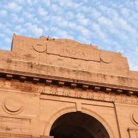 Low-angle view of the red sandstone India Gate arch and inscribed upper facade against a cloudy blue sky