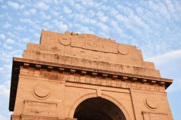 Low-angle view of the red sandstone India Gate arch and inscribed upper facade against a cloudy blue sky