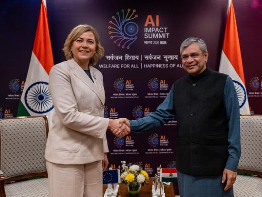 Ashwini Vaishnaw and Henna Virkkunen shake hands before an AI Impact Summit backdrop with Indian and EU flags.