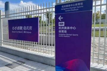 Asian Games slogan sign and Hangzhou Olympic Sports Centre stadium direction sign beside a white fence.