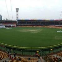 Panoramic view of a cricket stadium in Bengaluru with yellow seating, a green field and floodlight towers