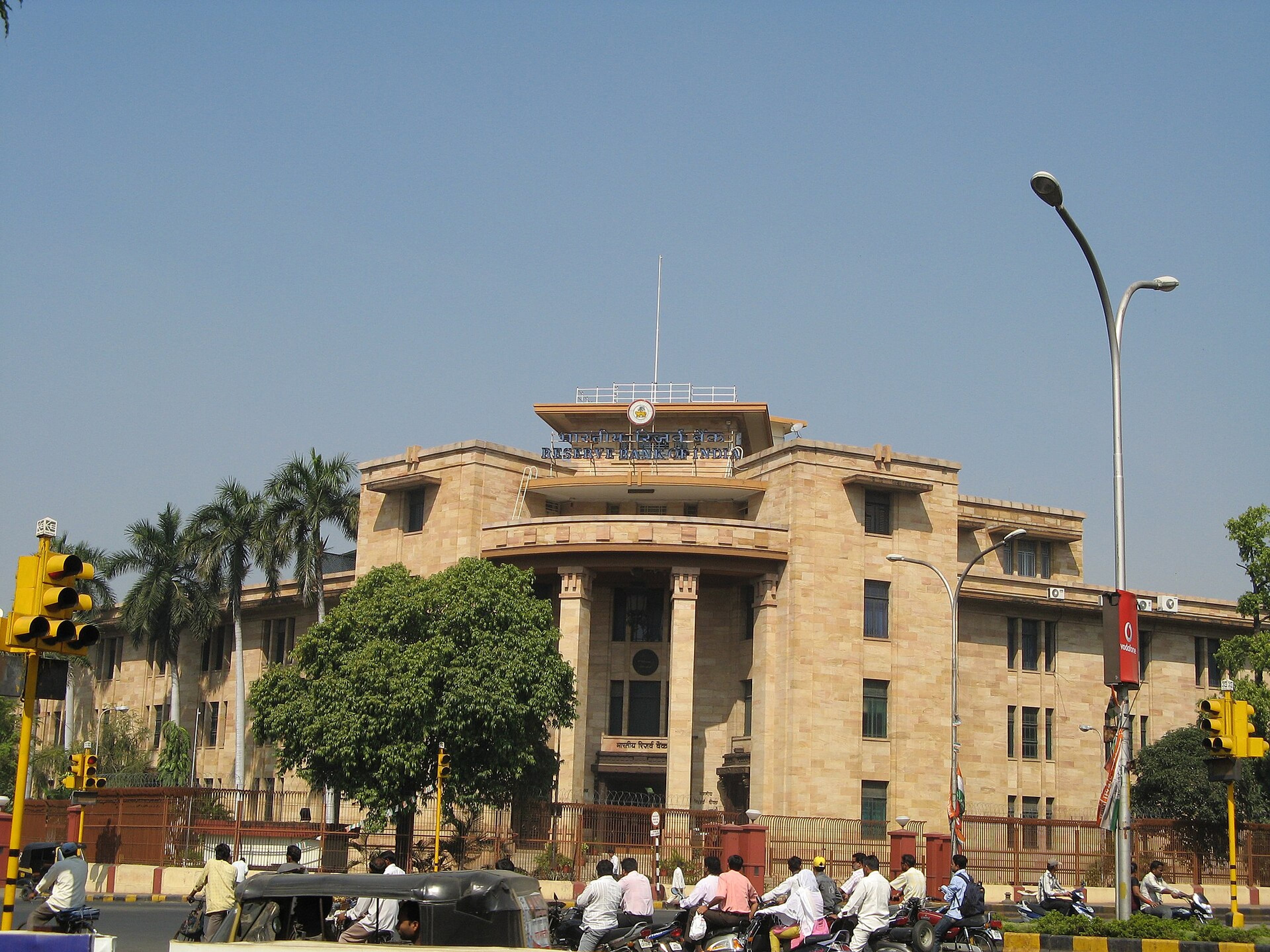 Reserve Bank of India building with a tan facade and central portico, with motorcycles and an auto-rickshaw on the street in front