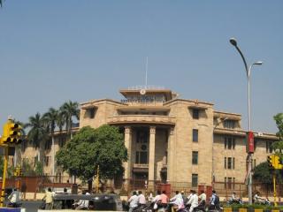 Reserve Bank of India building with a tan facade and central portico, with motorcycles and an auto-rickshaw on the street in front