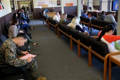 People sit on wooden benches in a waiting room, some filling out paperwork, at a tax assistance center.