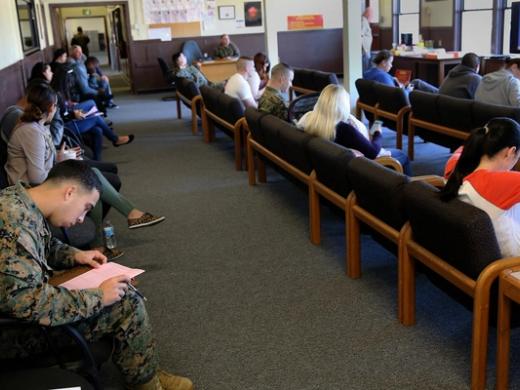 People sit on wooden benches in a waiting room, some filling out paperwork, at a tax assistance center.