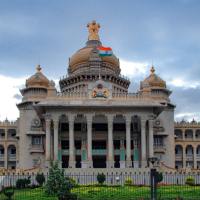 Facade of the Vidhana Soudha building in Bengaluru, with an Indian flag on its central dome under a cloudy sky