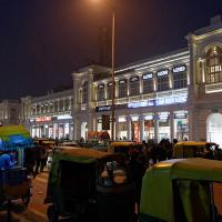 Lit colonnaded buildings at Connaught Place at night, with auto-rickshaws, a street food cart and people in the foreground