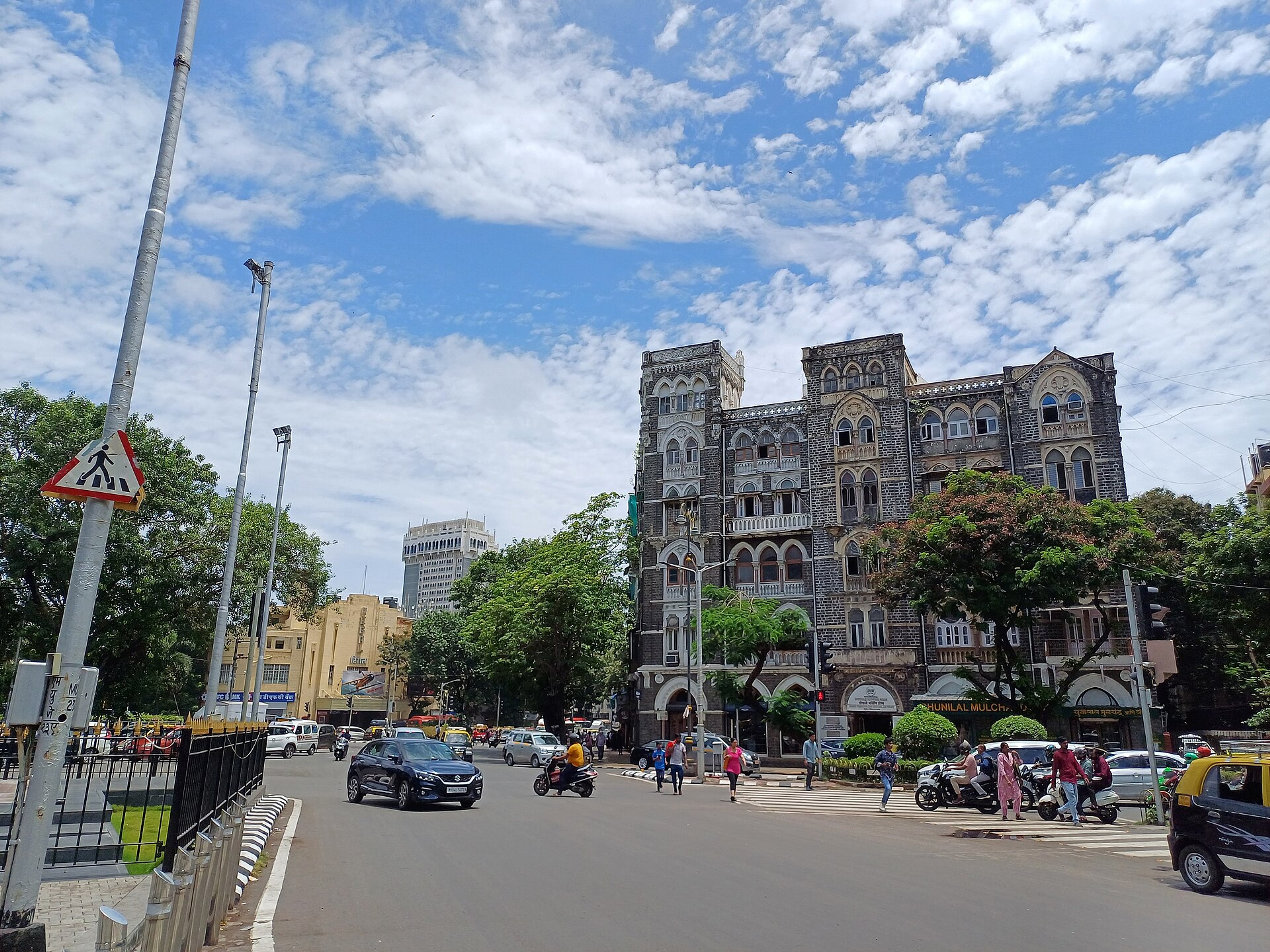 Mumbai street with traffic and pedestrians in front of a historic mansion, with a cinema at the far left.