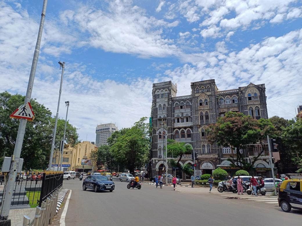 Mumbai street with traffic and pedestrians in front of a historic mansion, with a cinema at the far left.
