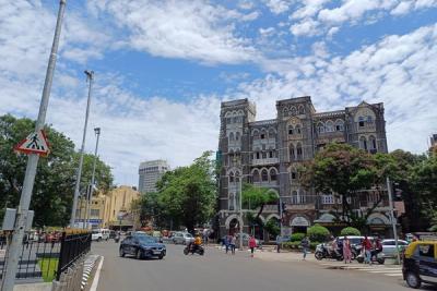 Mumbai street with traffic and pedestrians in front of a historic mansion, with a cinema at the far left.
