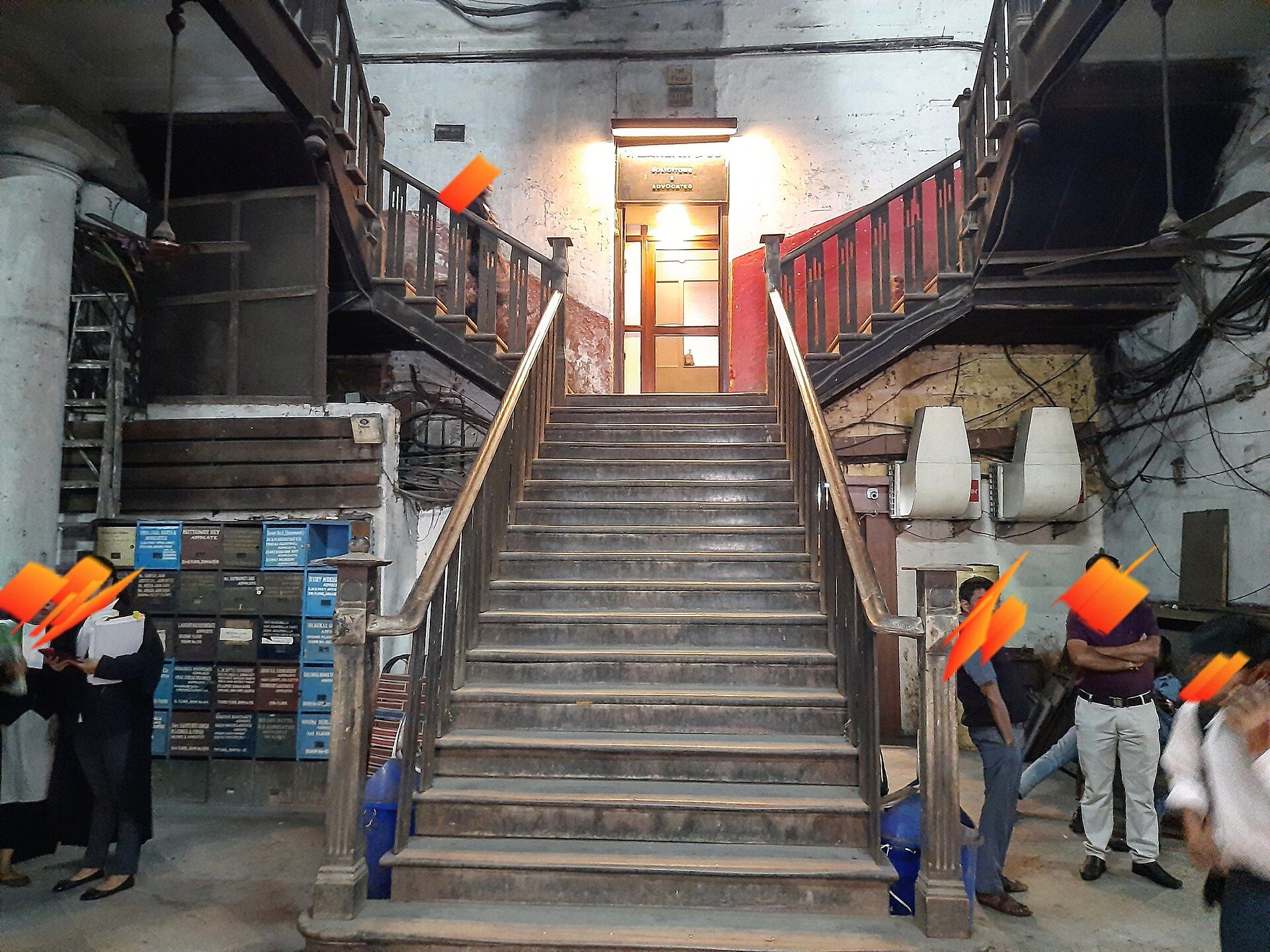 Wooden staircase leading to a lit doorway in a lawyers' chambers building, with people standing near lockers and boxes.