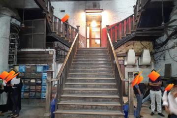 Wooden staircase leading to a lit doorway in a lawyers' chambers building, with people standing near lockers and boxes.