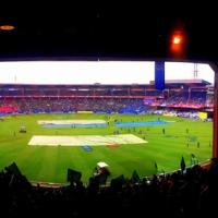 Panoramic view of the Chinnaswamy Stadium with the pitch covered by tarpaulins and crowds filling the stands.