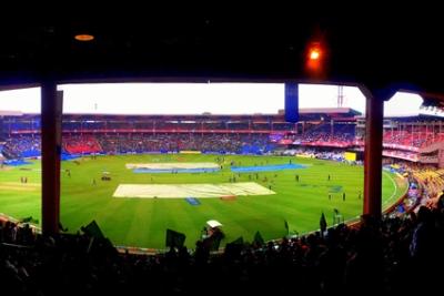 Panoramic view of the Chinnaswamy Stadium with the pitch covered by tarpaulins and crowds filling the stands.