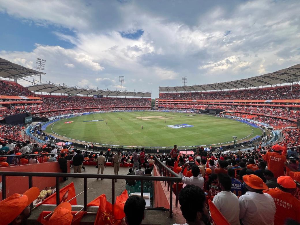 Crowd of orange-clad fans watches a cricket match from the stands at Rajiv Gandhi International Cricket Stadium.